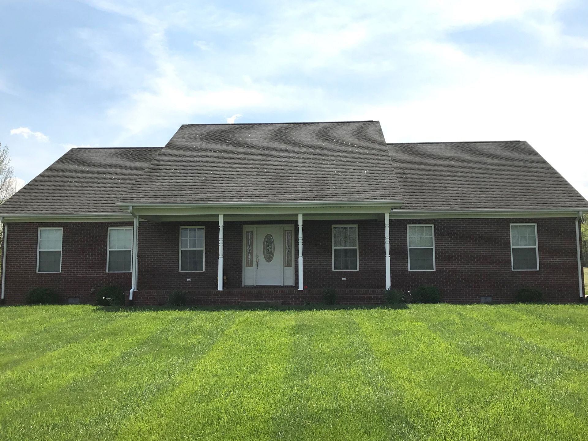 Single-story brick house with a gray roof and white front door on a green lawn