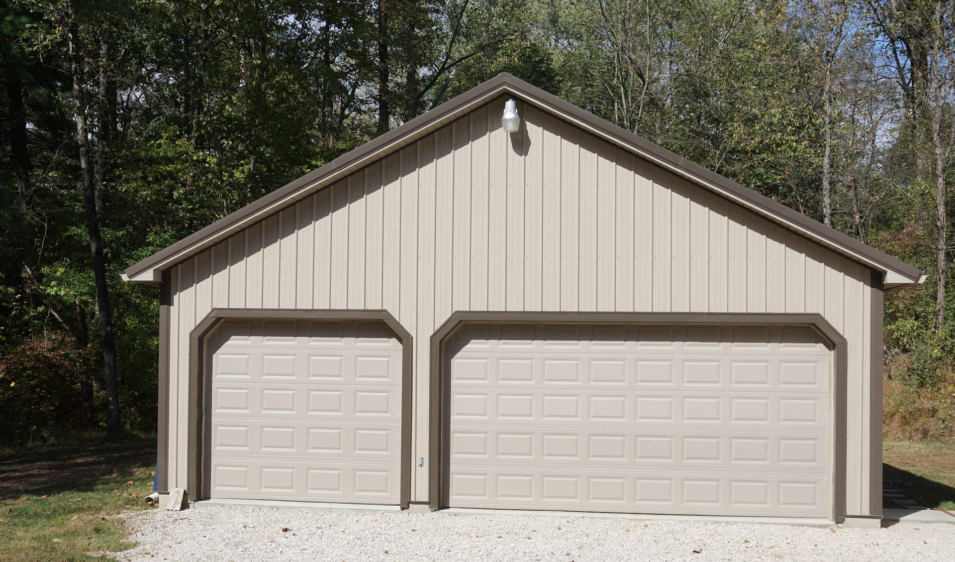 Beige two-car garage with brown trim and double doors, set in a wooded yard.
