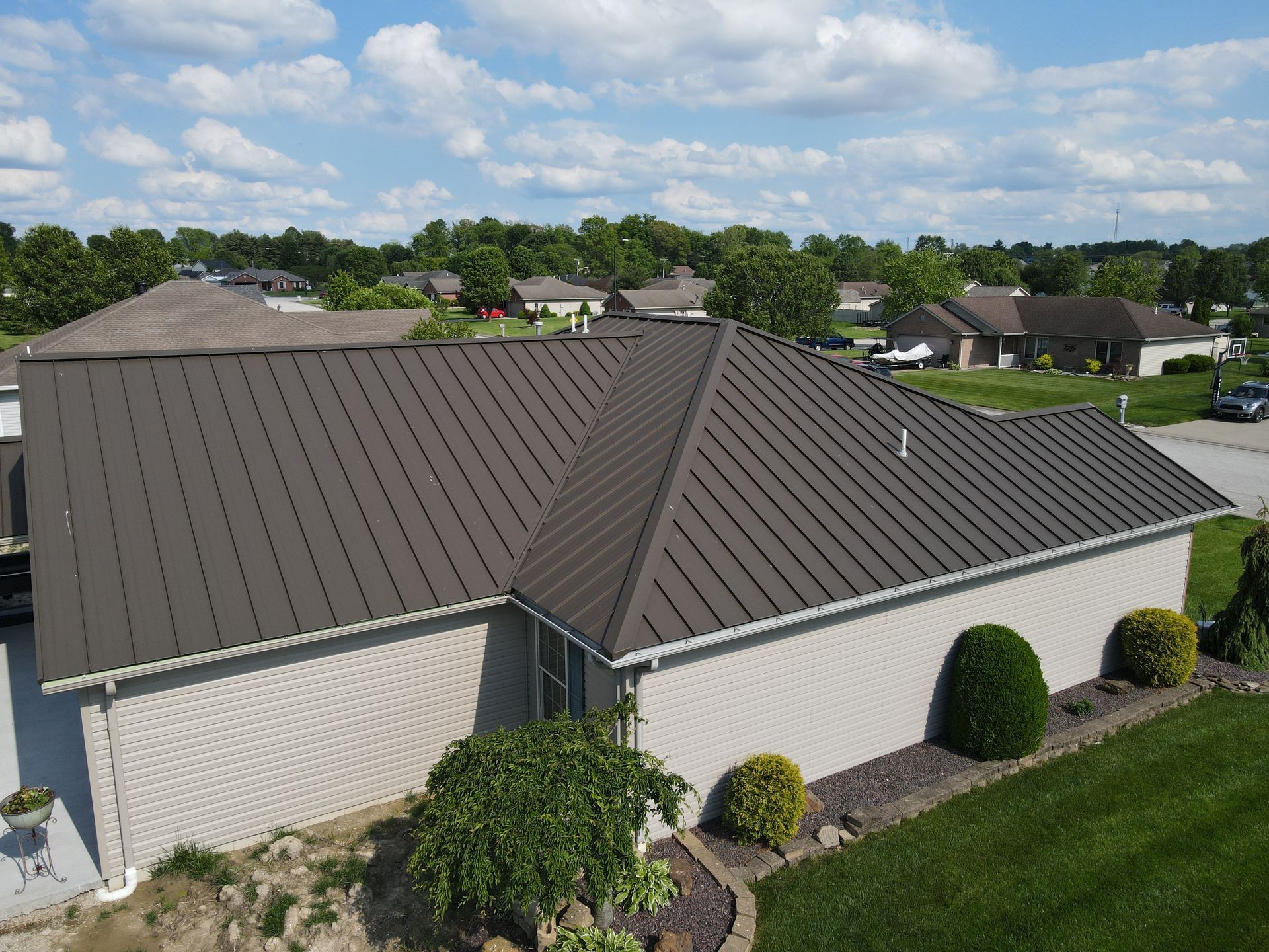 Suburban house with gray metal roof, white brick walls, and manicured lawn under a clear sky