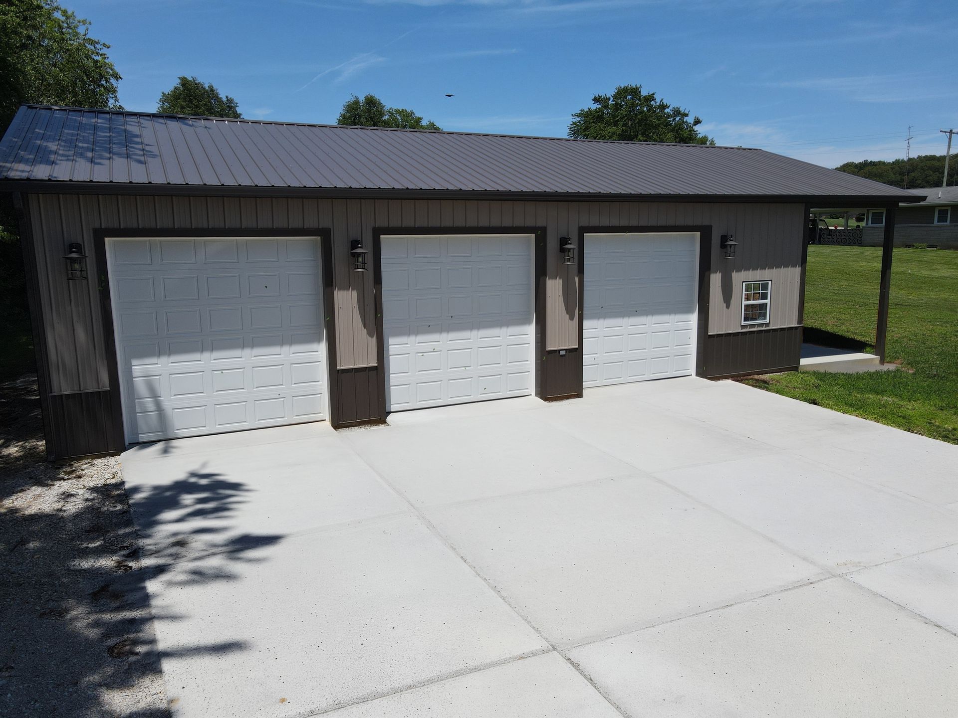 Three-car garage with white doors, dark siding, and a metal roof beside a concrete driveway.