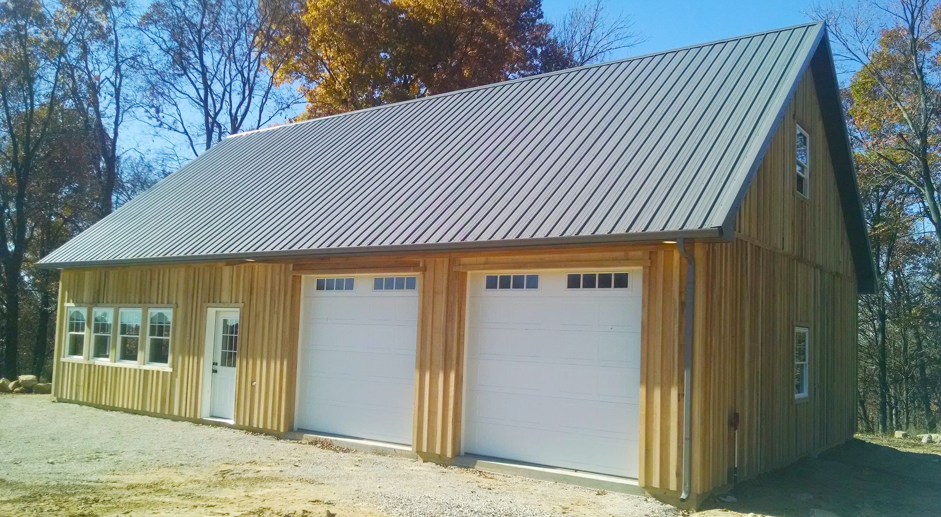 Tan barn with metal roof and two white garage doors in a sunny rural setting