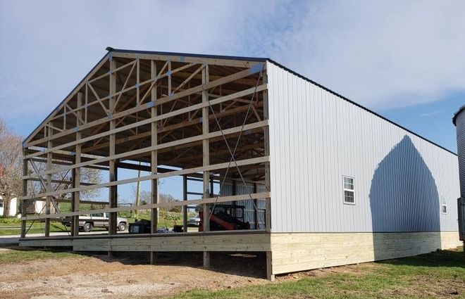 Open-sided white barn with exposed wooden roof framing on a raised foundation