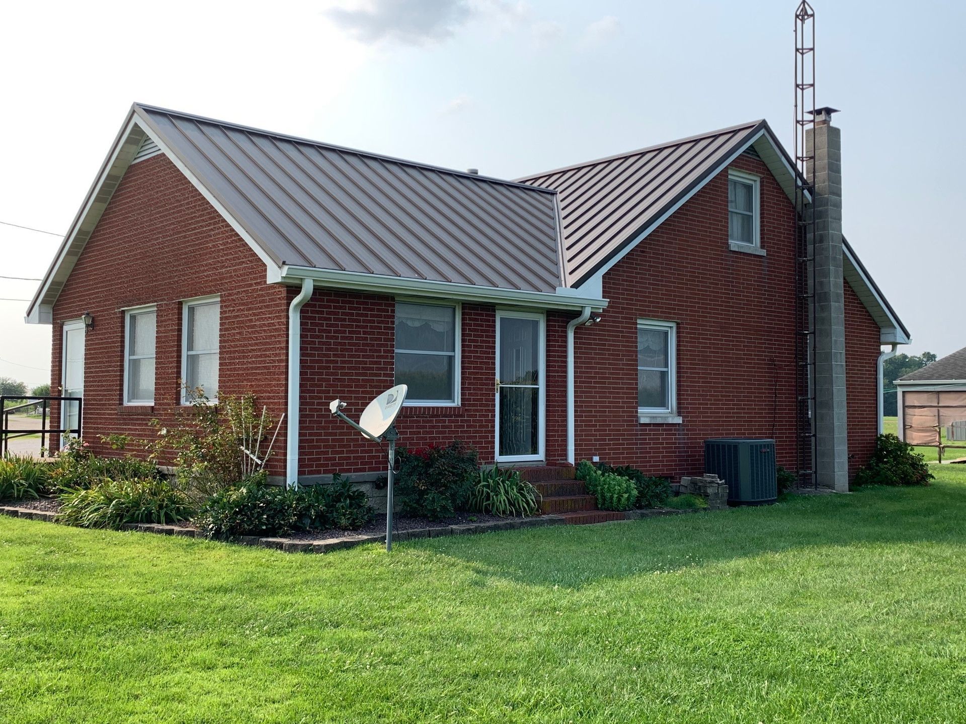 Red brick house with gray metal roof and green lawn, viewed from the front yard.