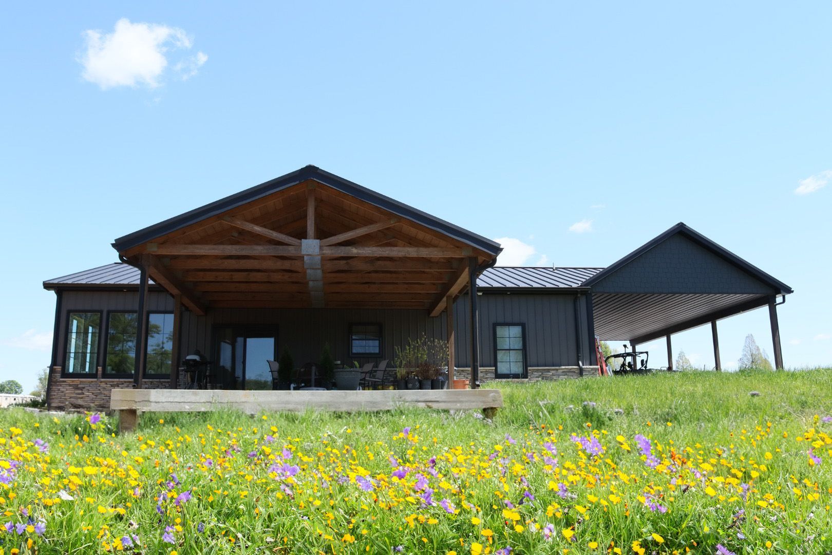Rustic cabin with a covered porch in a wildflower meadow under a clear blue sky