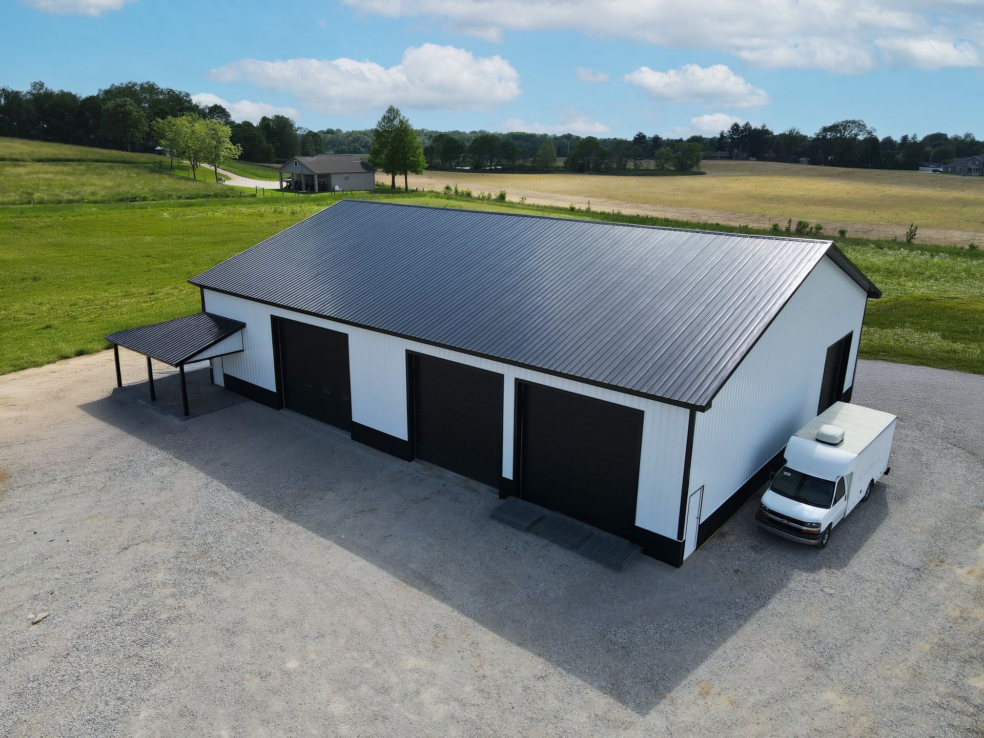 White barn with black roof and doors on a gravel lot, with a pickup truck beside it in open countryside.