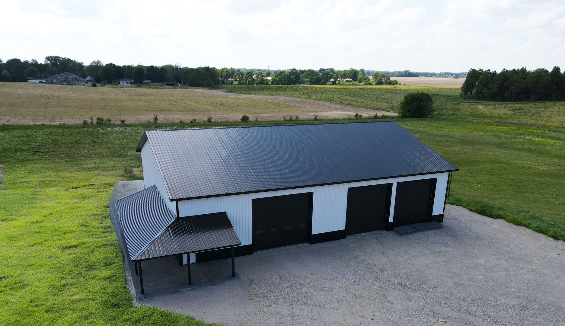 Modern black-and-white outbuilding with a metal roof beside gravel, set in open farmland fields