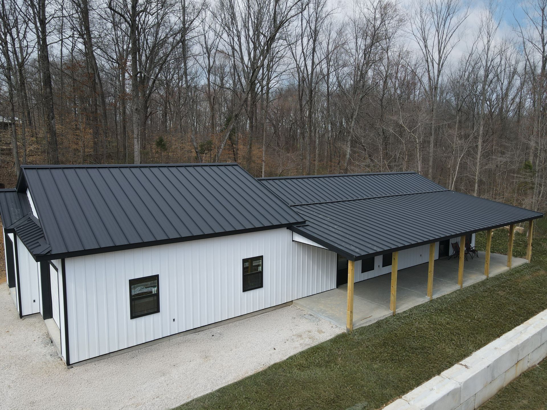 White metal barn-style building with dark roof and yellow posts beside a road in a wooded area