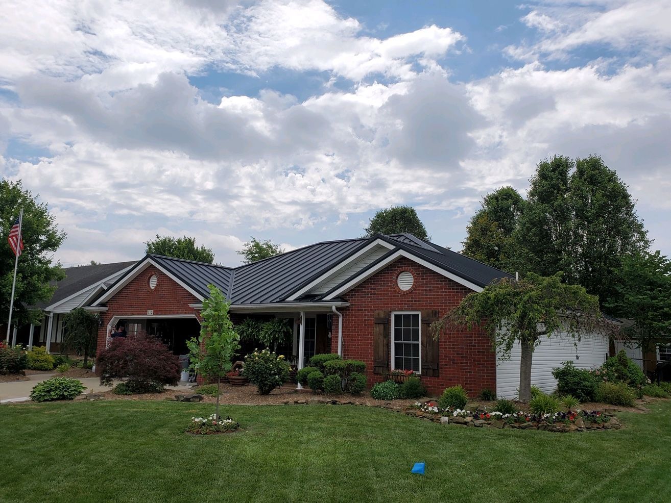 Brick house with a dark roof, front lawn, and trees under a cloudy sky