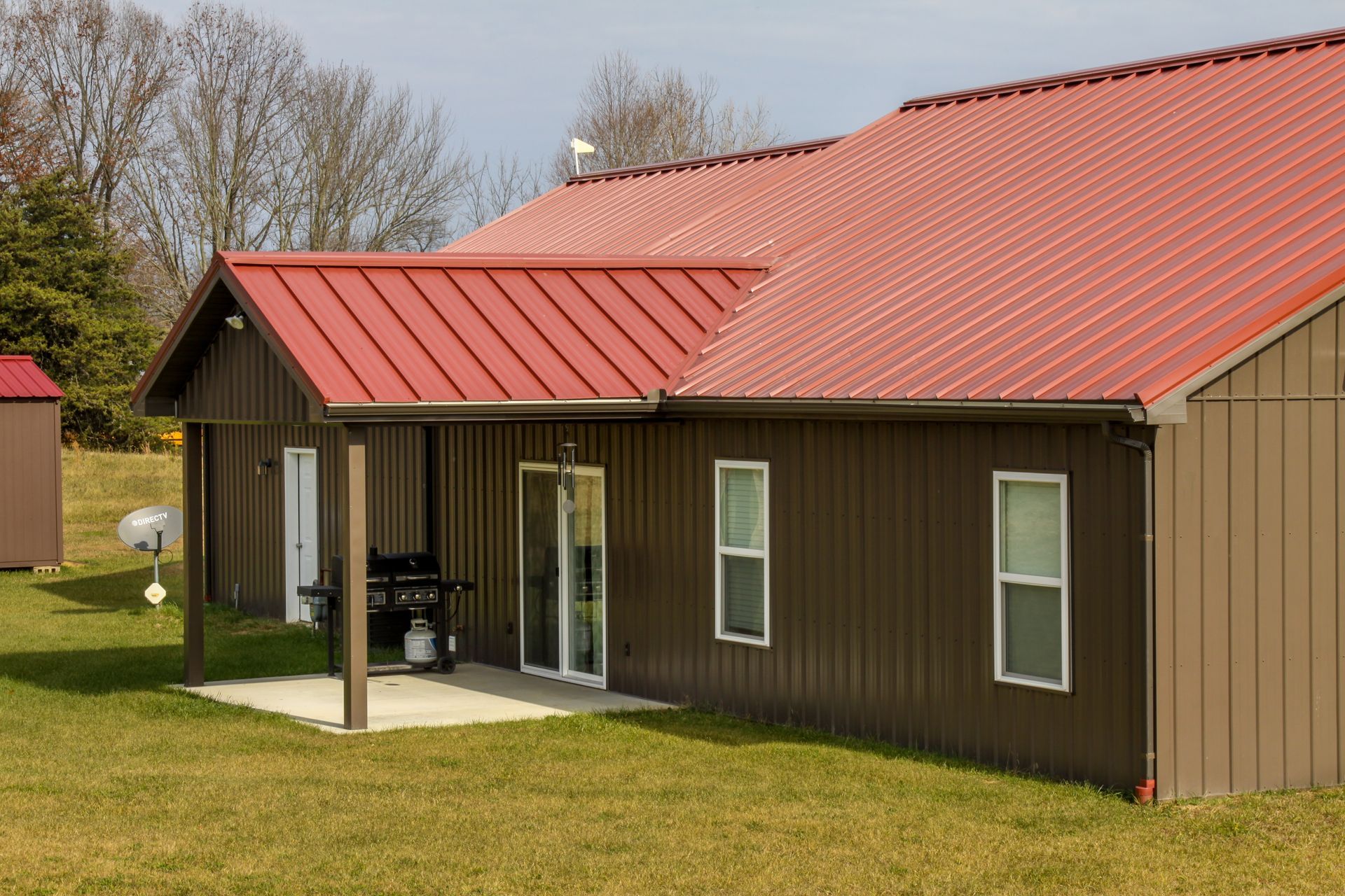 Brown house with red metal roof and covered porch on a grassy lawn