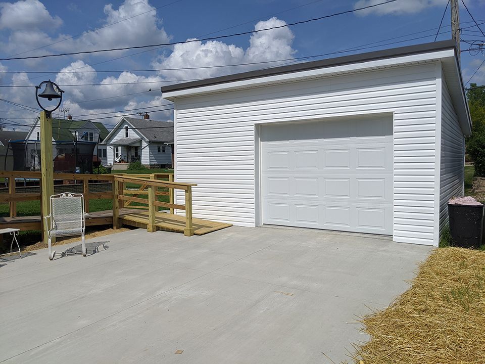 White detached garage with a paved driveway and wooden fence under a partly cloudy sky