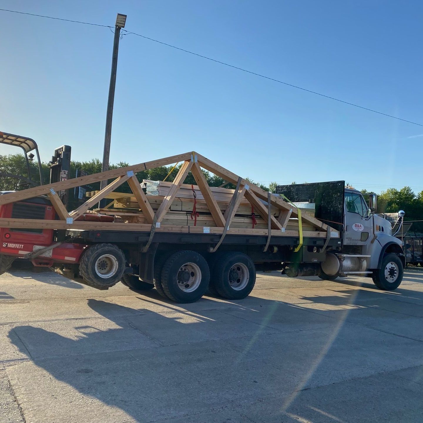 Flatbed truck carrying a wooden truss structure in a sunny parking lot