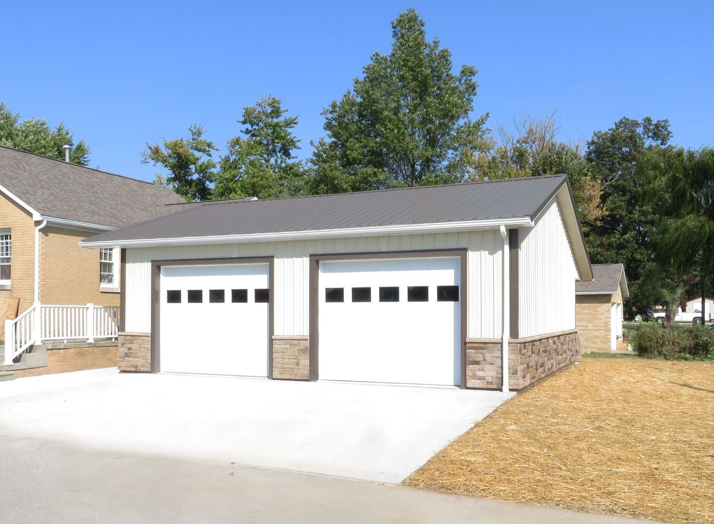 Two-car white garage with stone accents and a wide concrete driveway in a suburban neighborhood