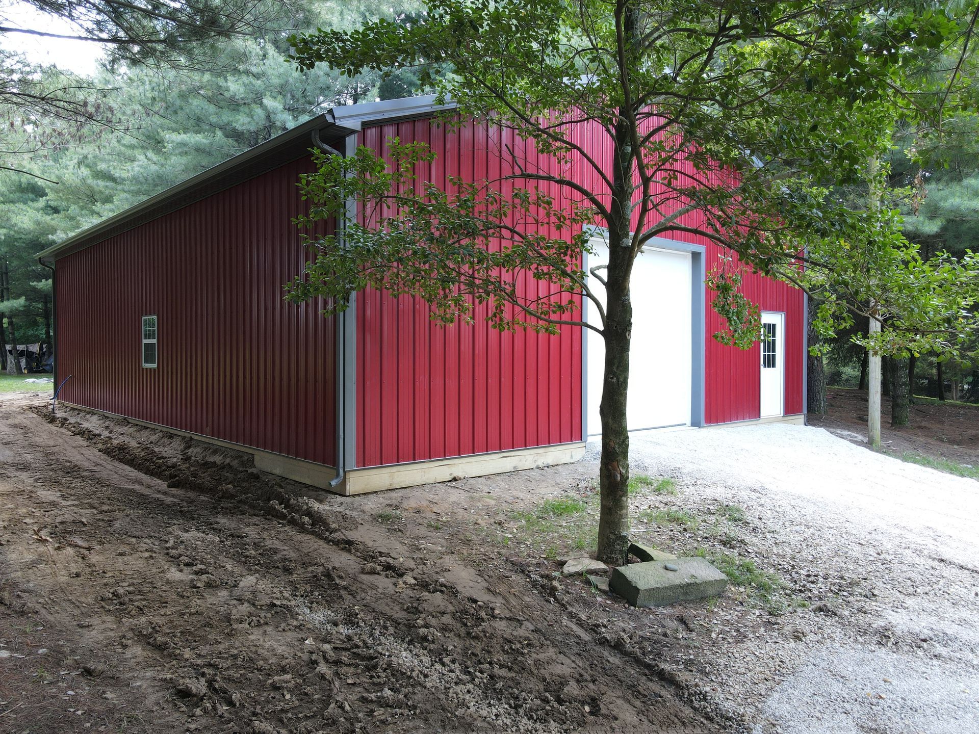 Red metal barn with white doors beside a gravel path in a wooded area