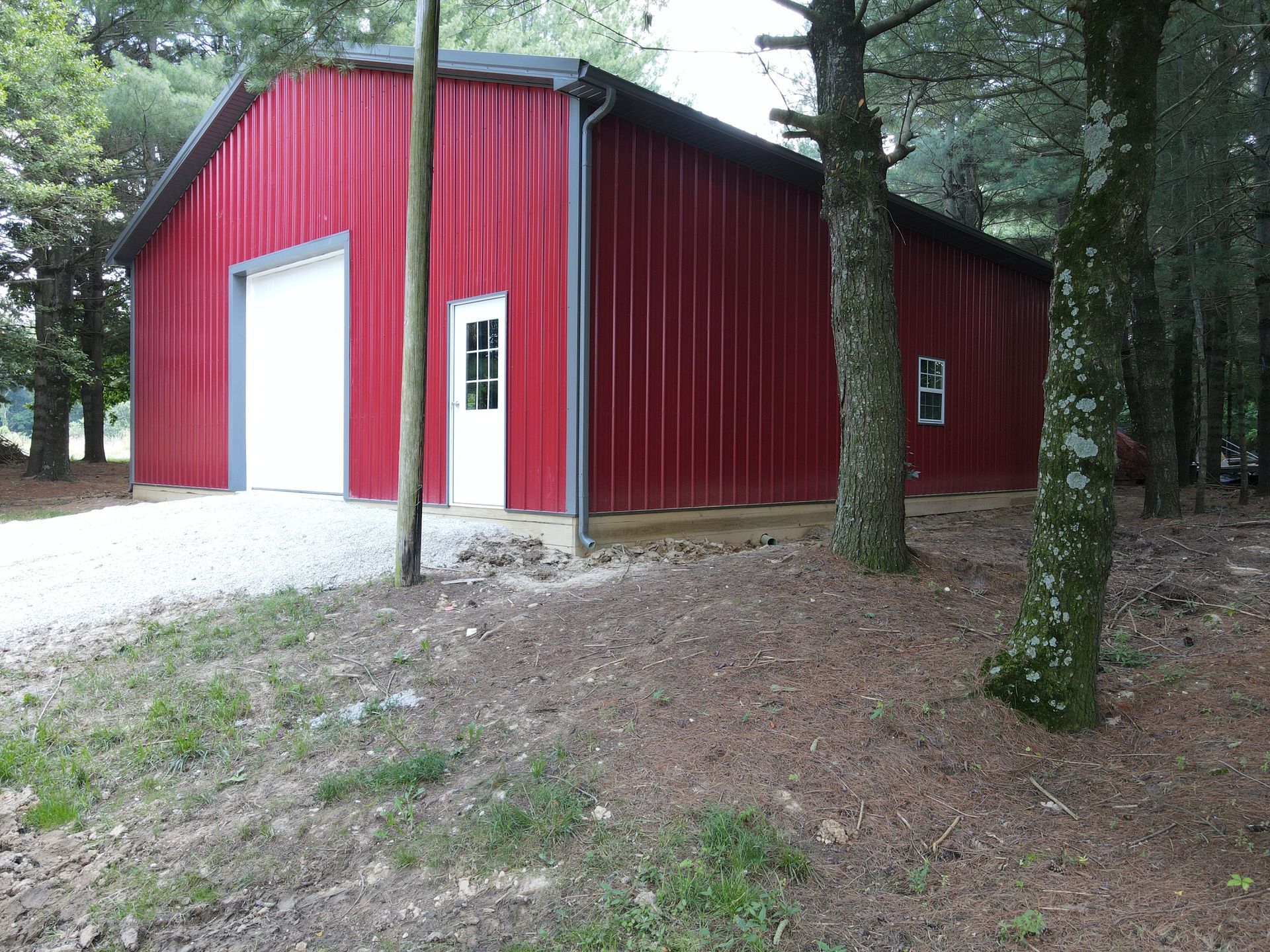 Red metal barn-like building with white doors in a wooded area