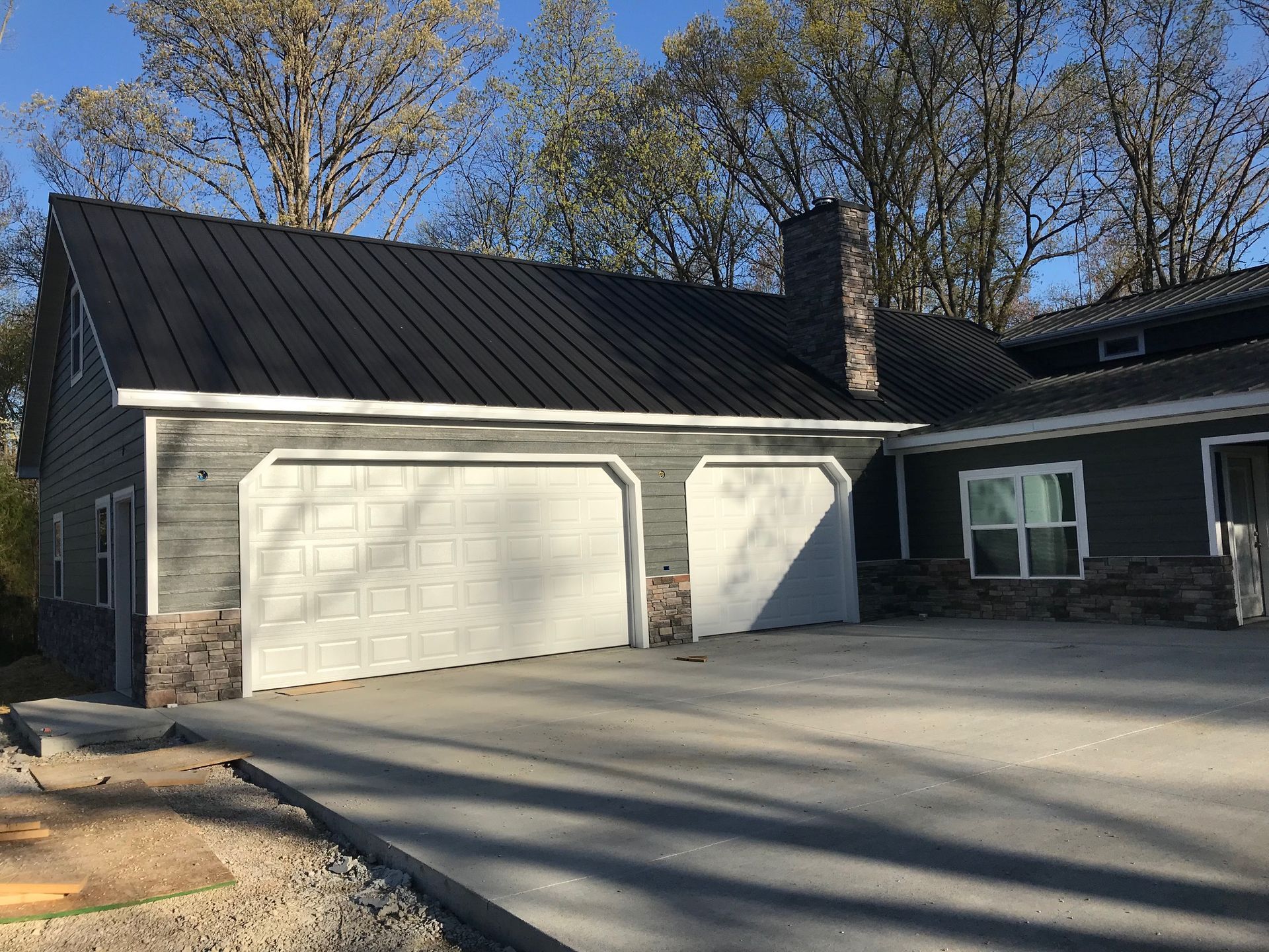 Two-car garage with dark roof, white doors, and a paved driveway in front of a gray house