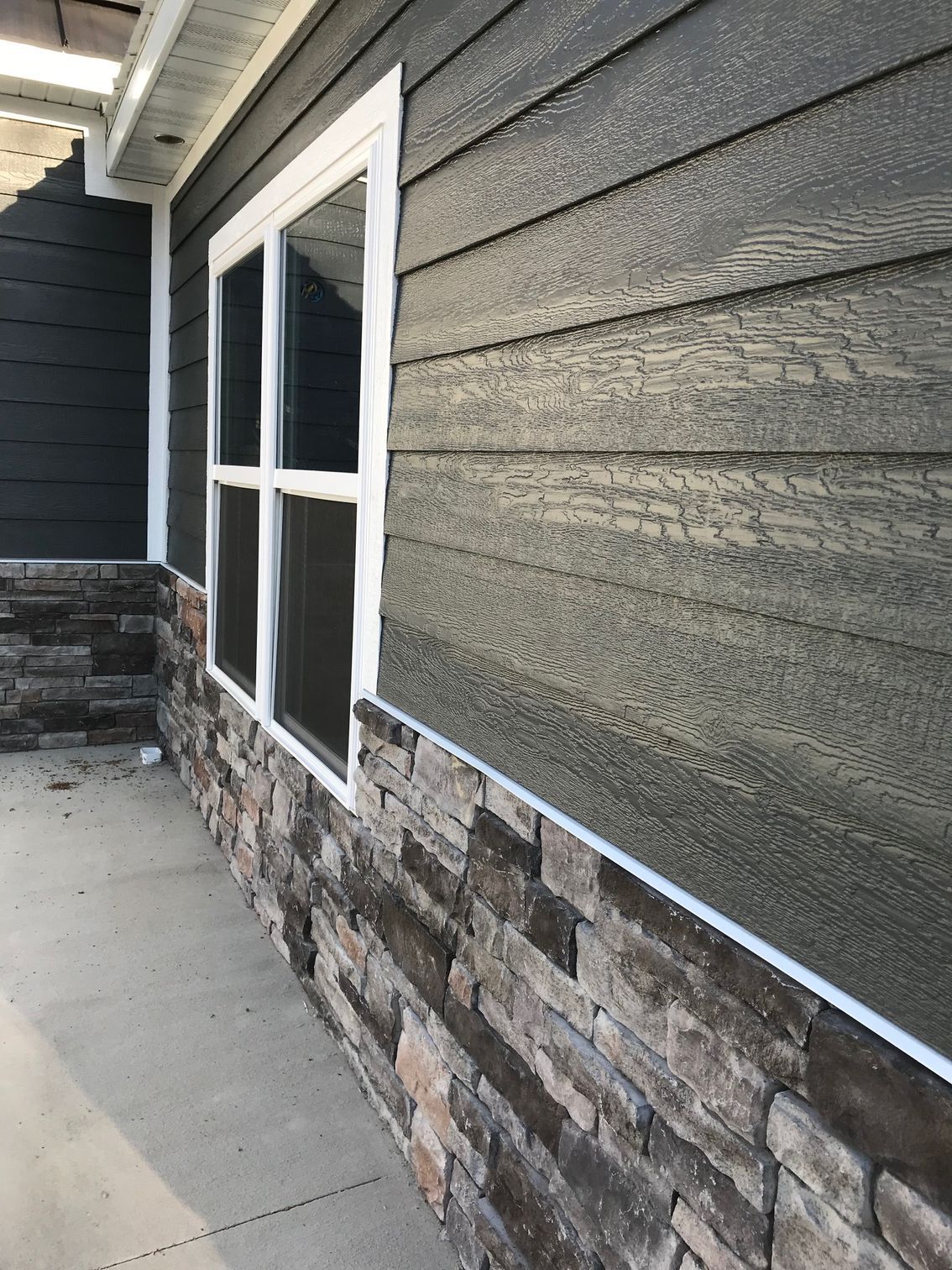 Apartment exterior with stone facade, gray siding, and a window beside a concrete walkway