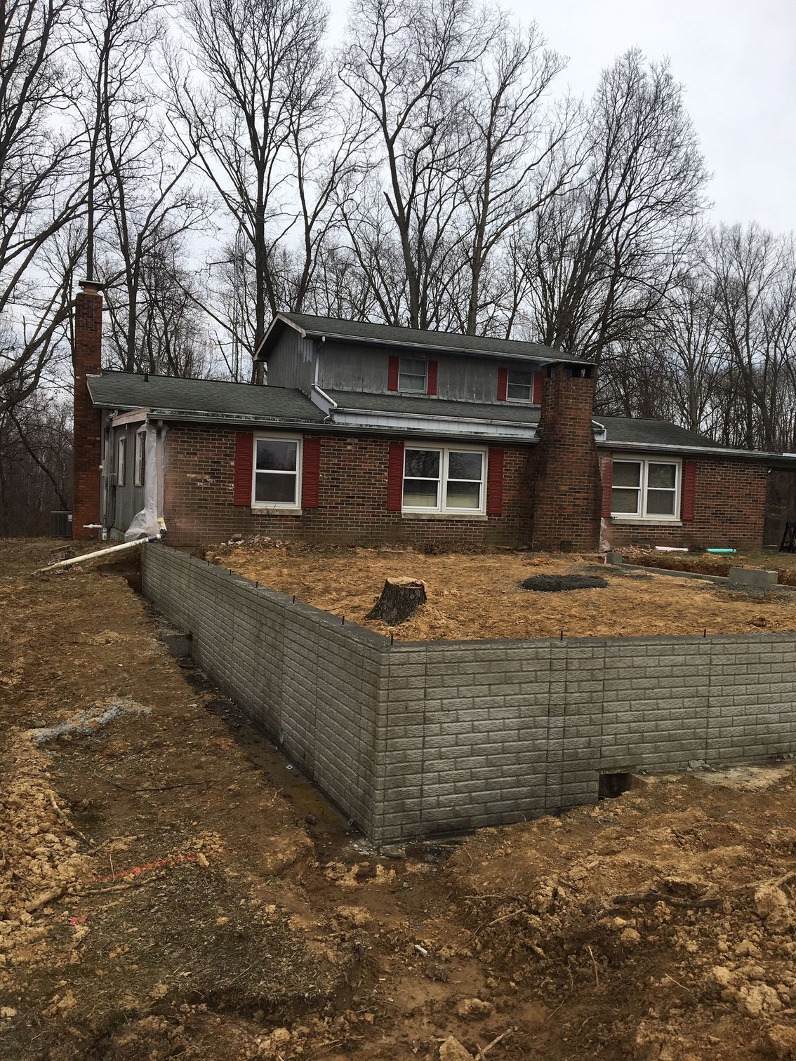 Small red house with a gray roof and stone retaining wall on a muddy hillside in winter.