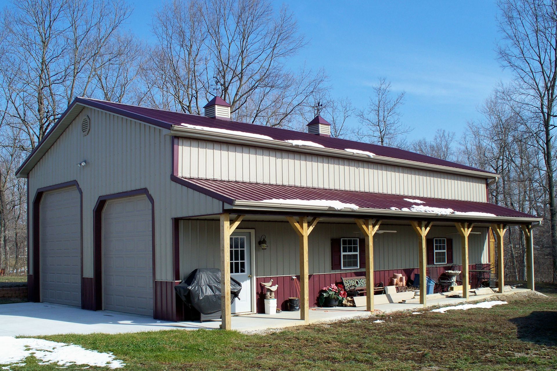 Small beige barn with large garage doors and a covered porch in a grassy rural setting