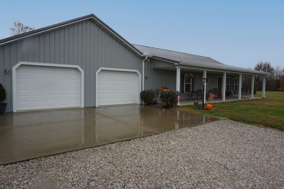 Gray house with double garage, wet driveway, and front porch beside gravel yard