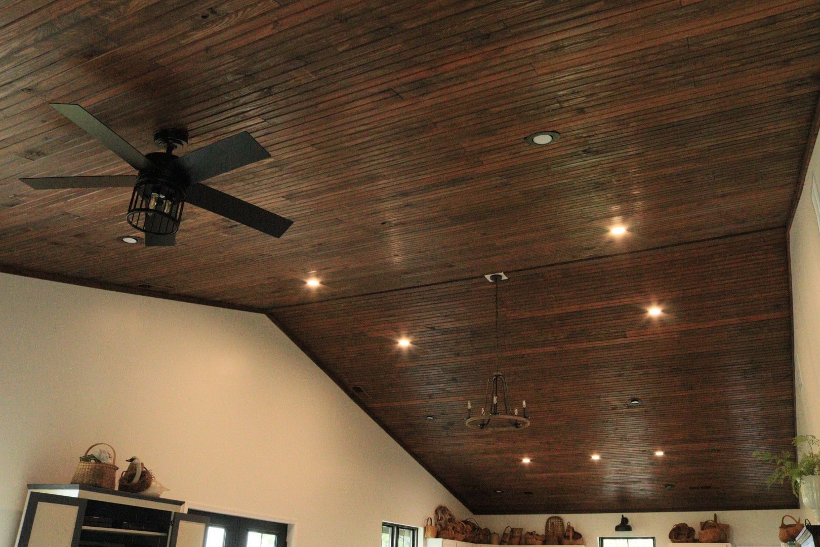 Wood-paneled ceiling with recessed lights and a black ceiling fan in a room