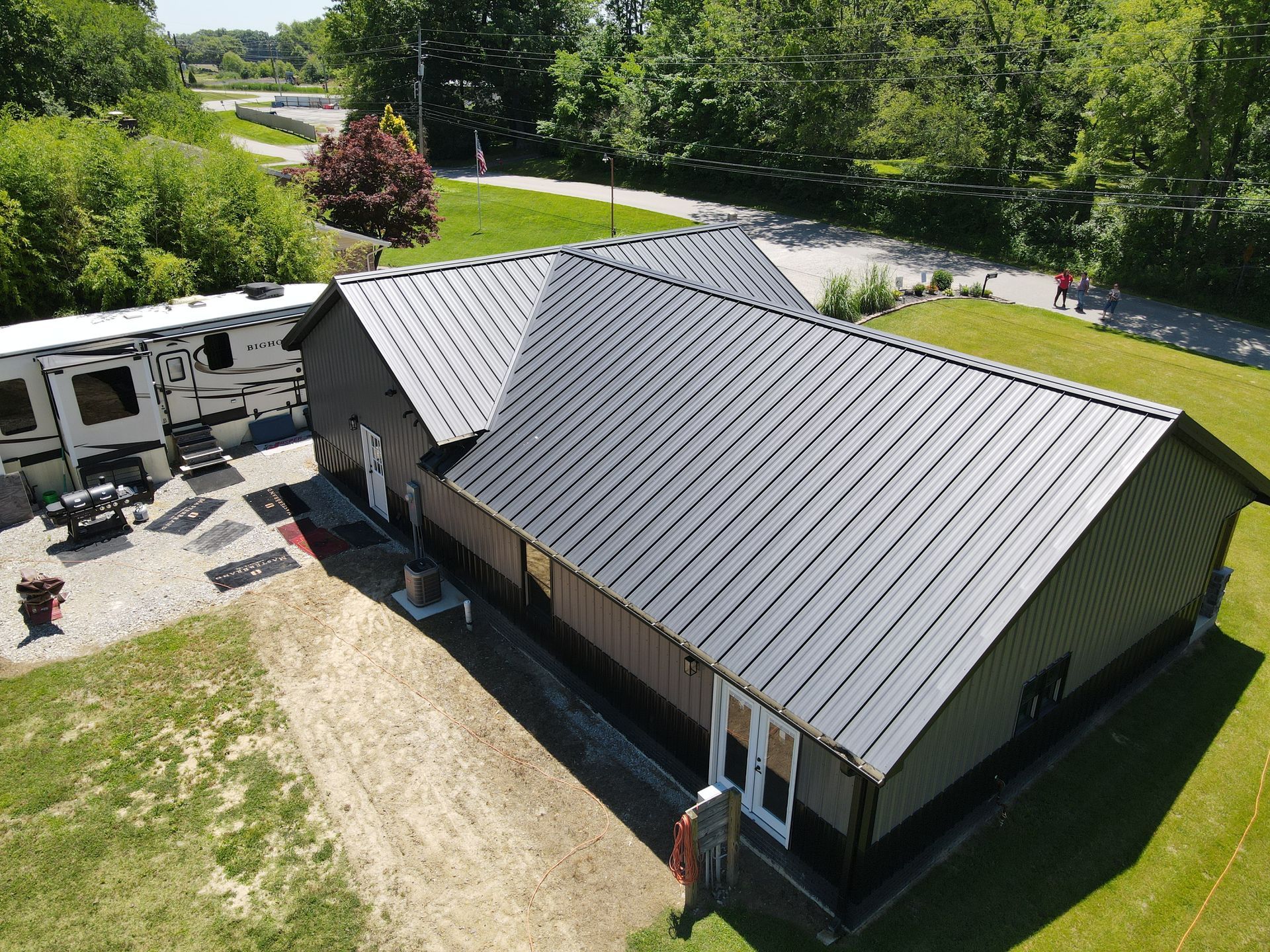 Aerial view of a gray-roofed building beside a paved courtyard and green lawn, near a road and trees.