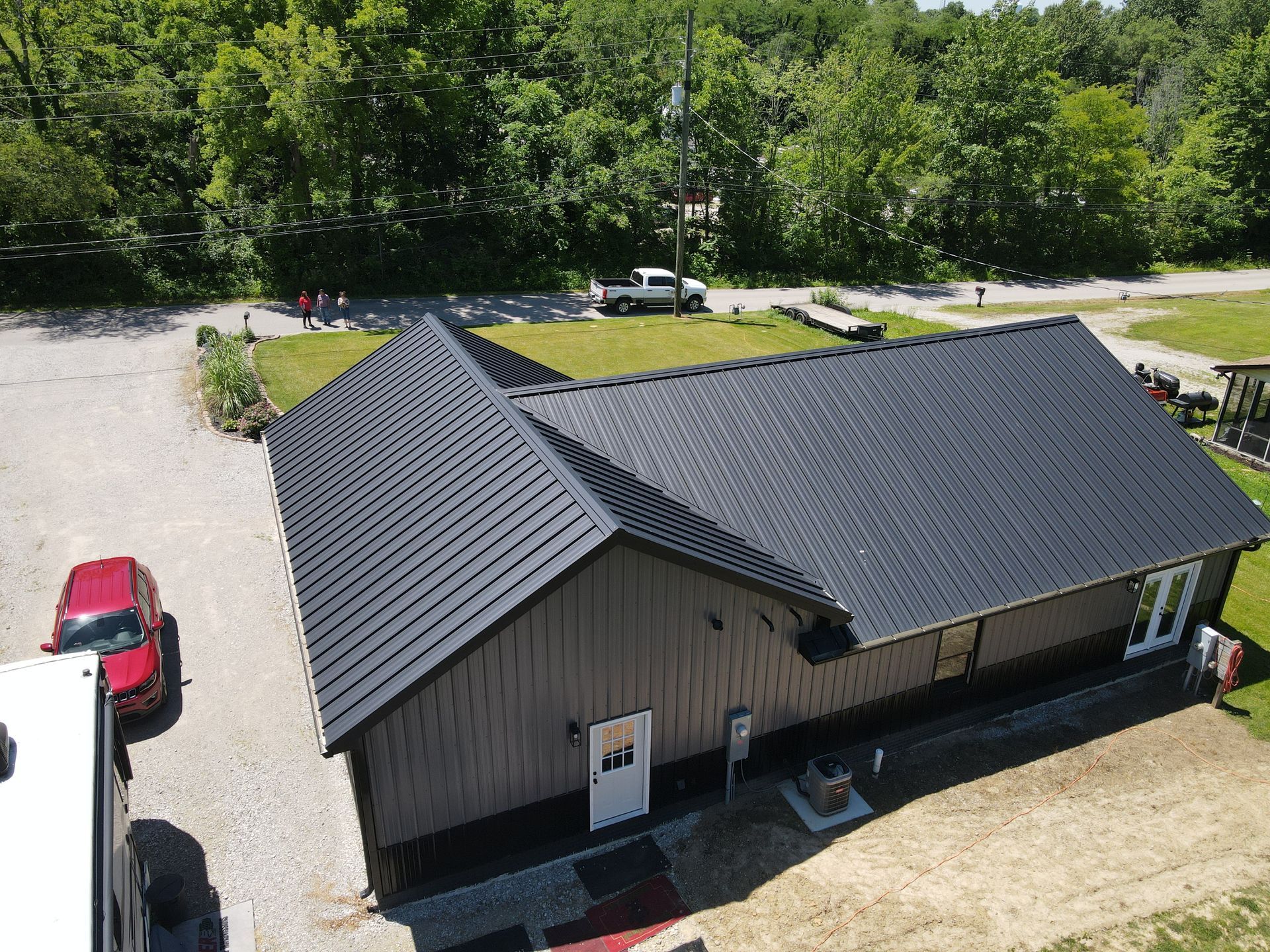 Aerial view of a small gray house with a dark roof, surrounded by gravel, grass, and trees.