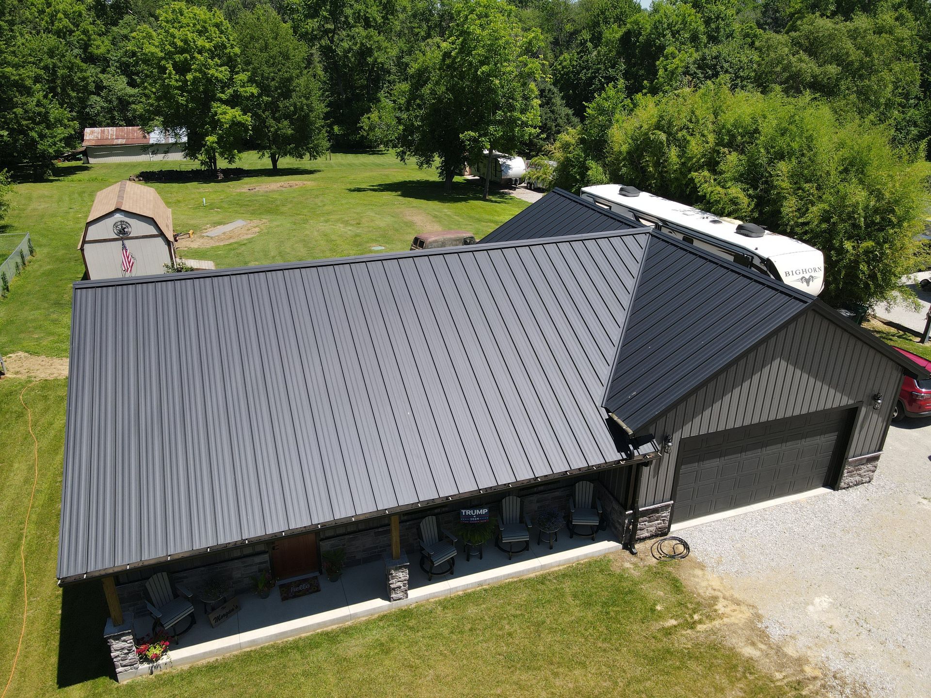 Aerial view of a gray metal-roofed house with a gravel driveway and trees around it