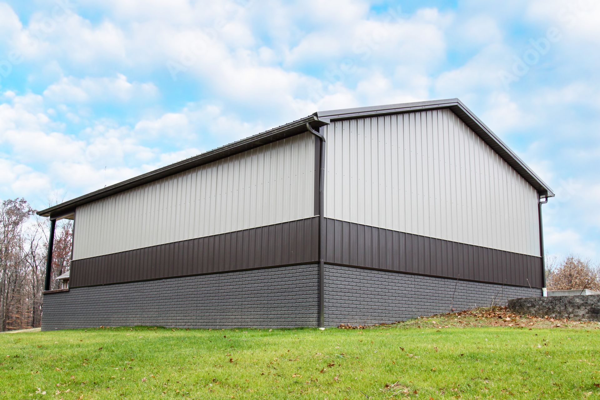 Large white and gray metal barn on a grassy field under a partly cloudy sky