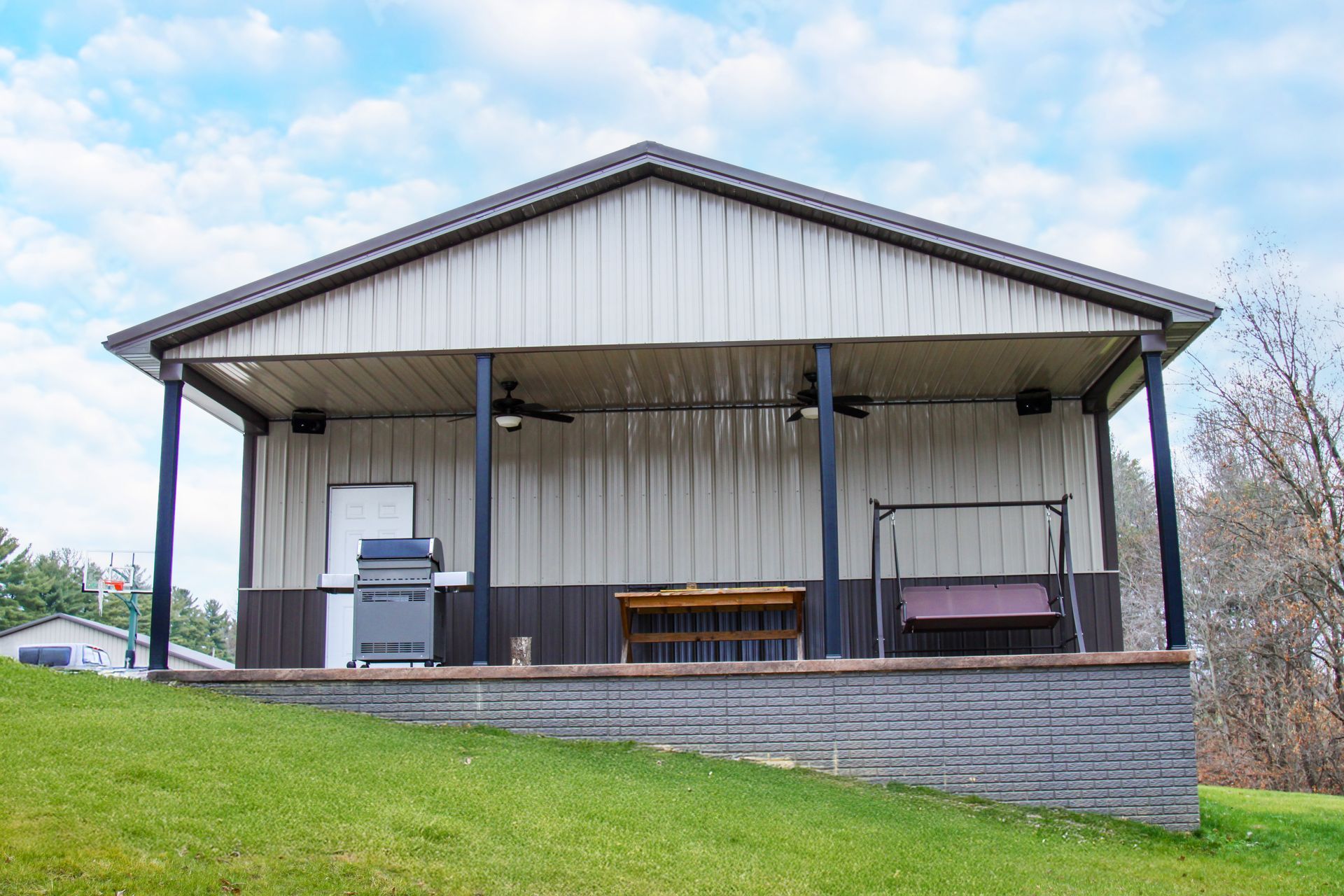 Outdoor pavilion with a metal roof, picnic tables, and a grill on a grassy hillside
