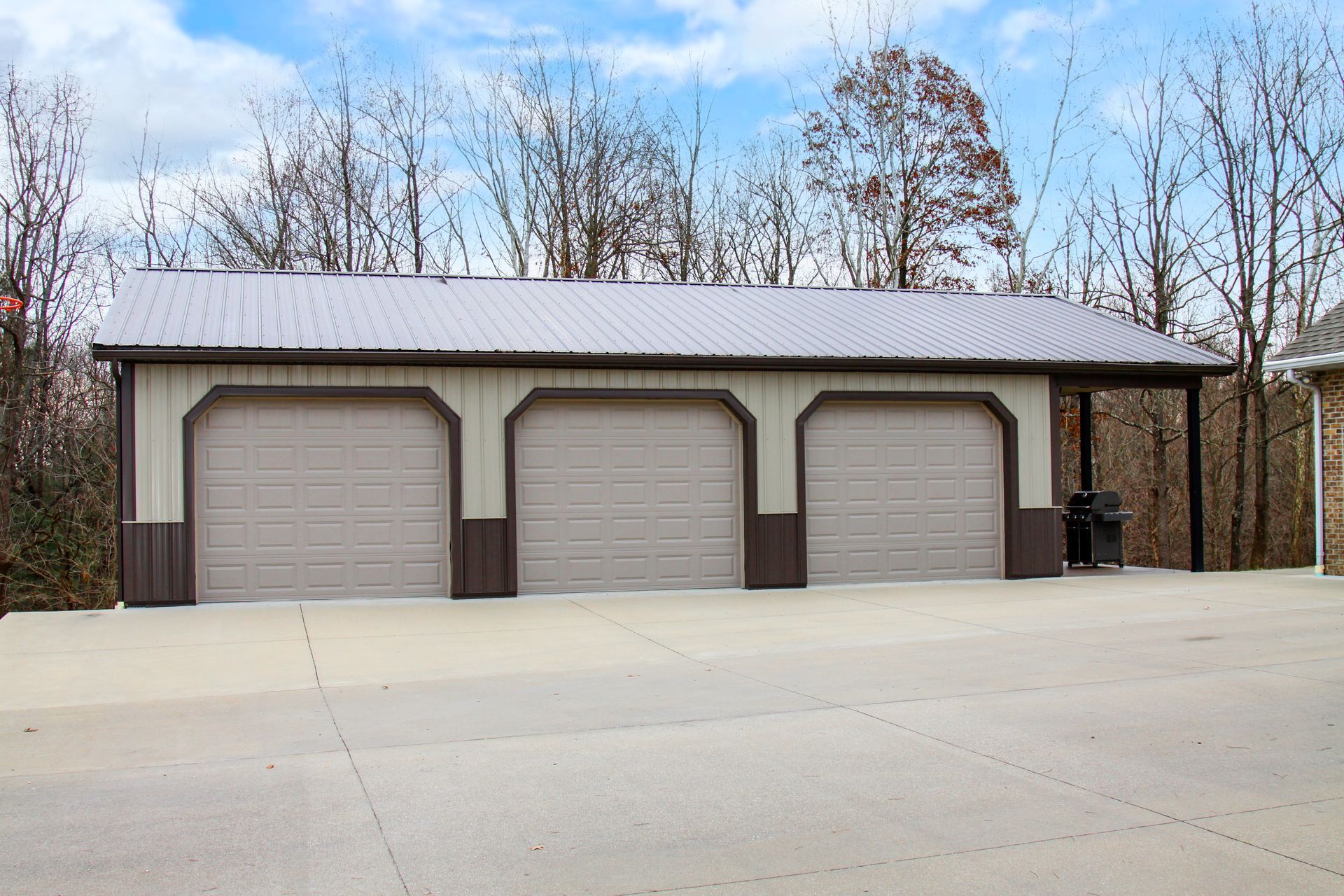 Three-bay tan garage with brown trim beside a paved driveway and leafless trees