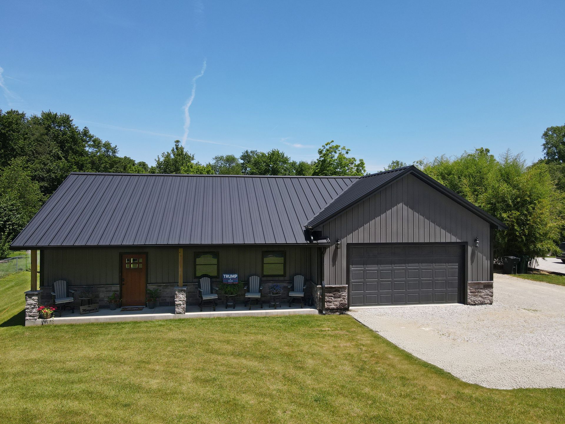 Single-story gray house with black roof, front porch, and attached garage on a sunny day
