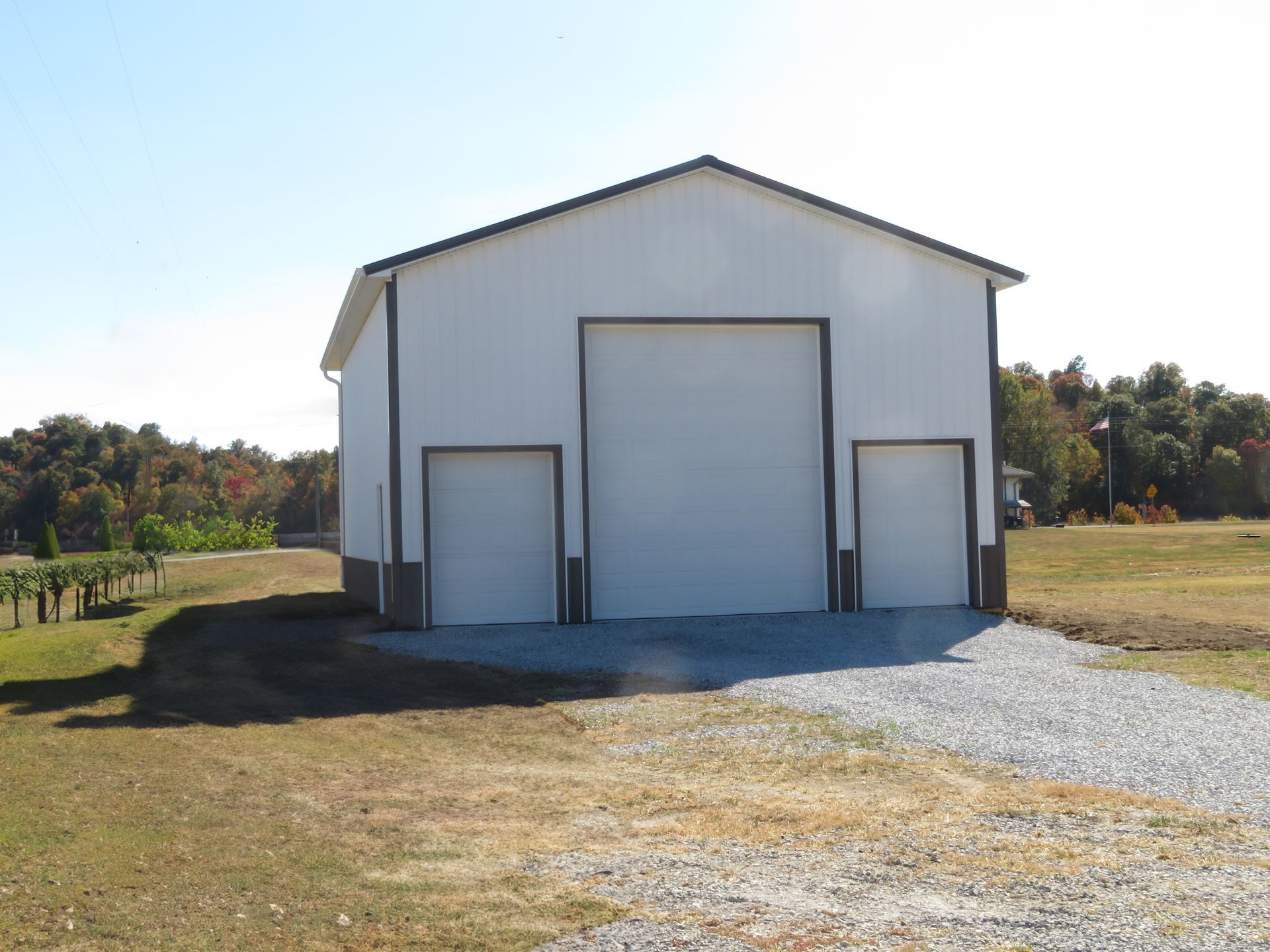 White metal barn with large central door, small side doors, and gravel driveway in a rural field.