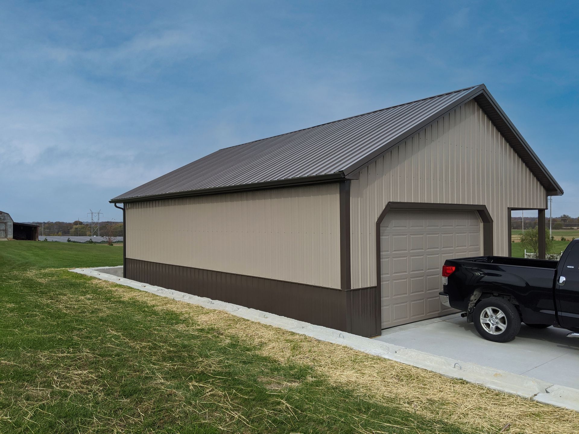 Tan-sided detached garage with a gray roof and black truck parked beside it on a driveway.