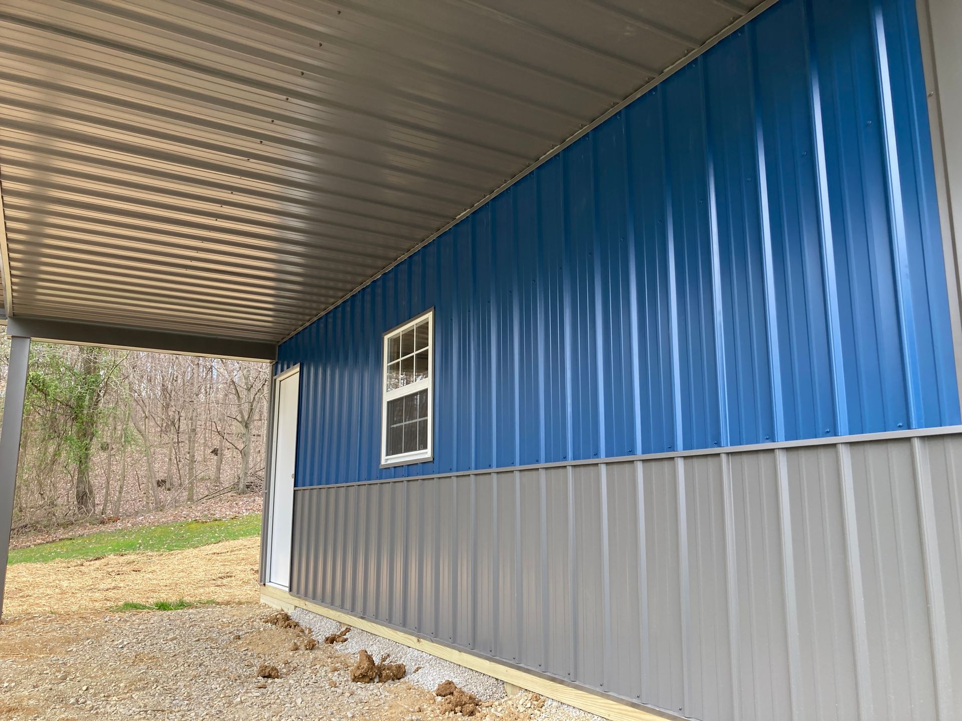 Blue and gray metal building exterior with a covered porch and a small window side wall