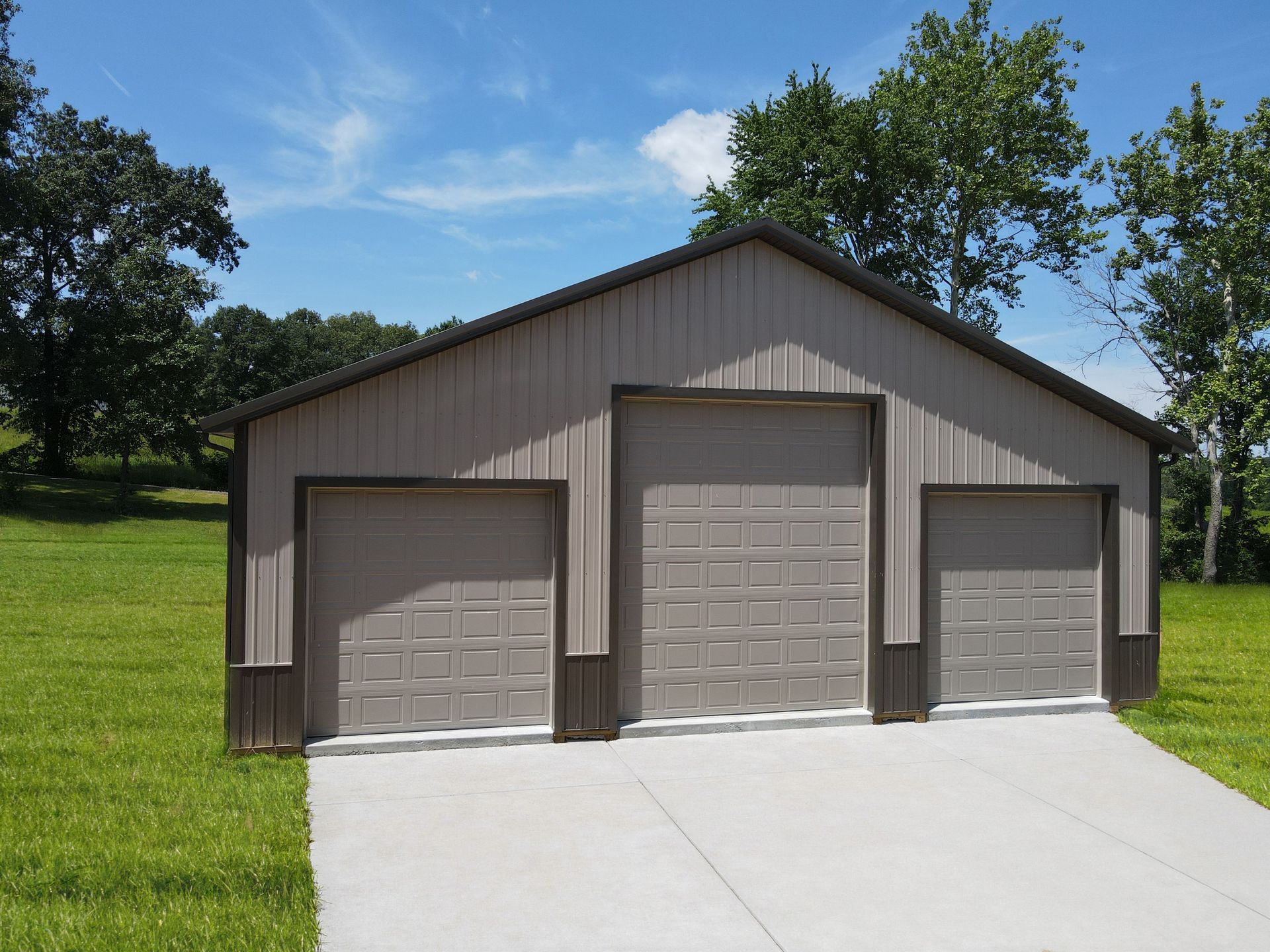 Three-bay metal garage with tan doors and a concrete driveway on a grassy lawn