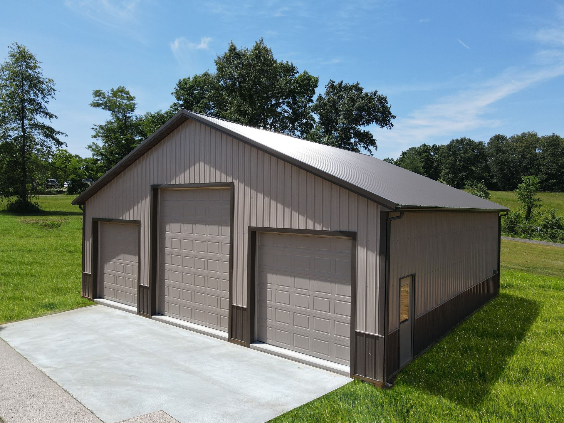 Brown metal three-bay garage with beige doors on a concrete slab in a grassy yard