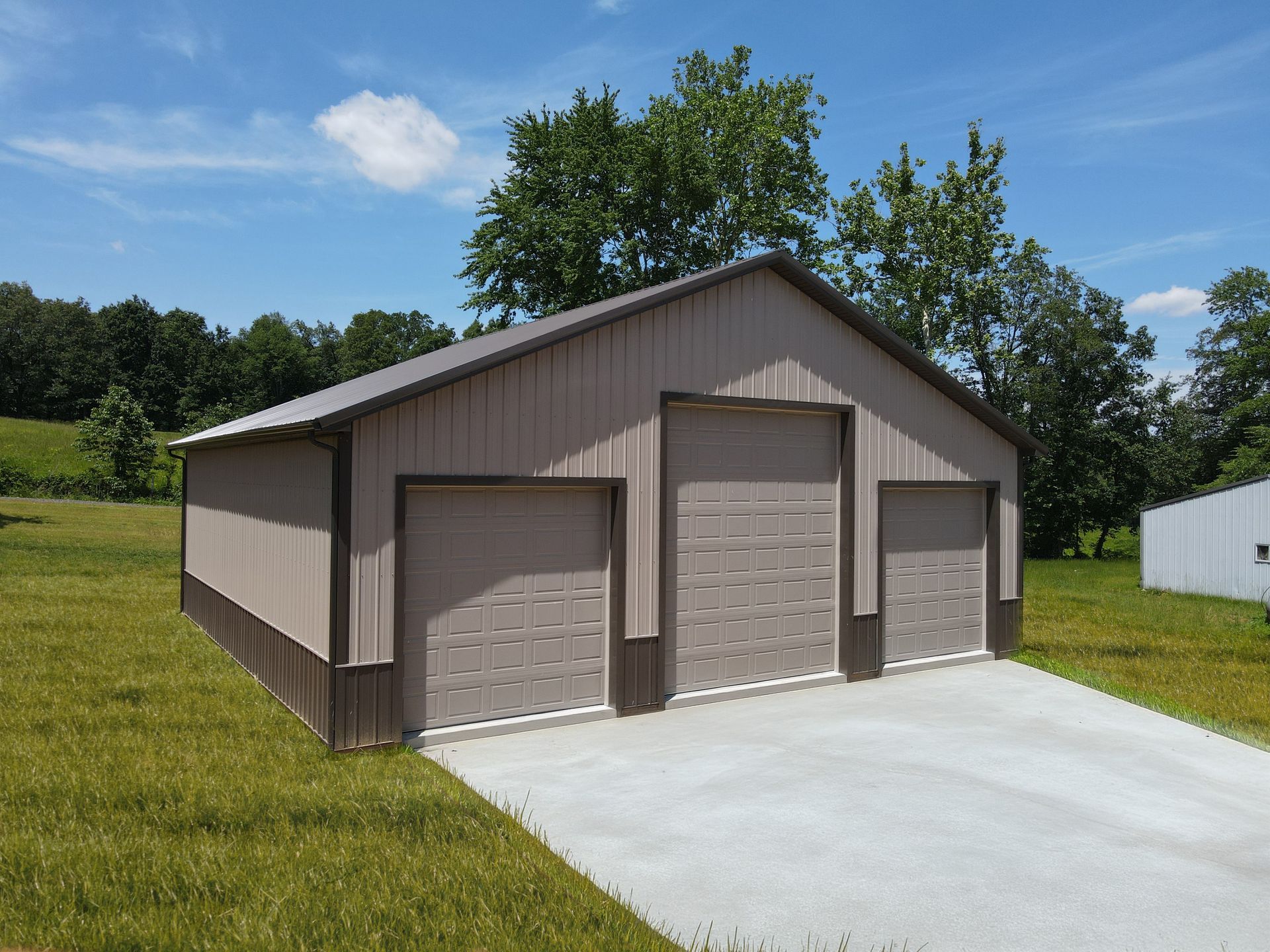 Brown detached two-car garage with beige doors and concrete driveway on a grassy lot under blue sky