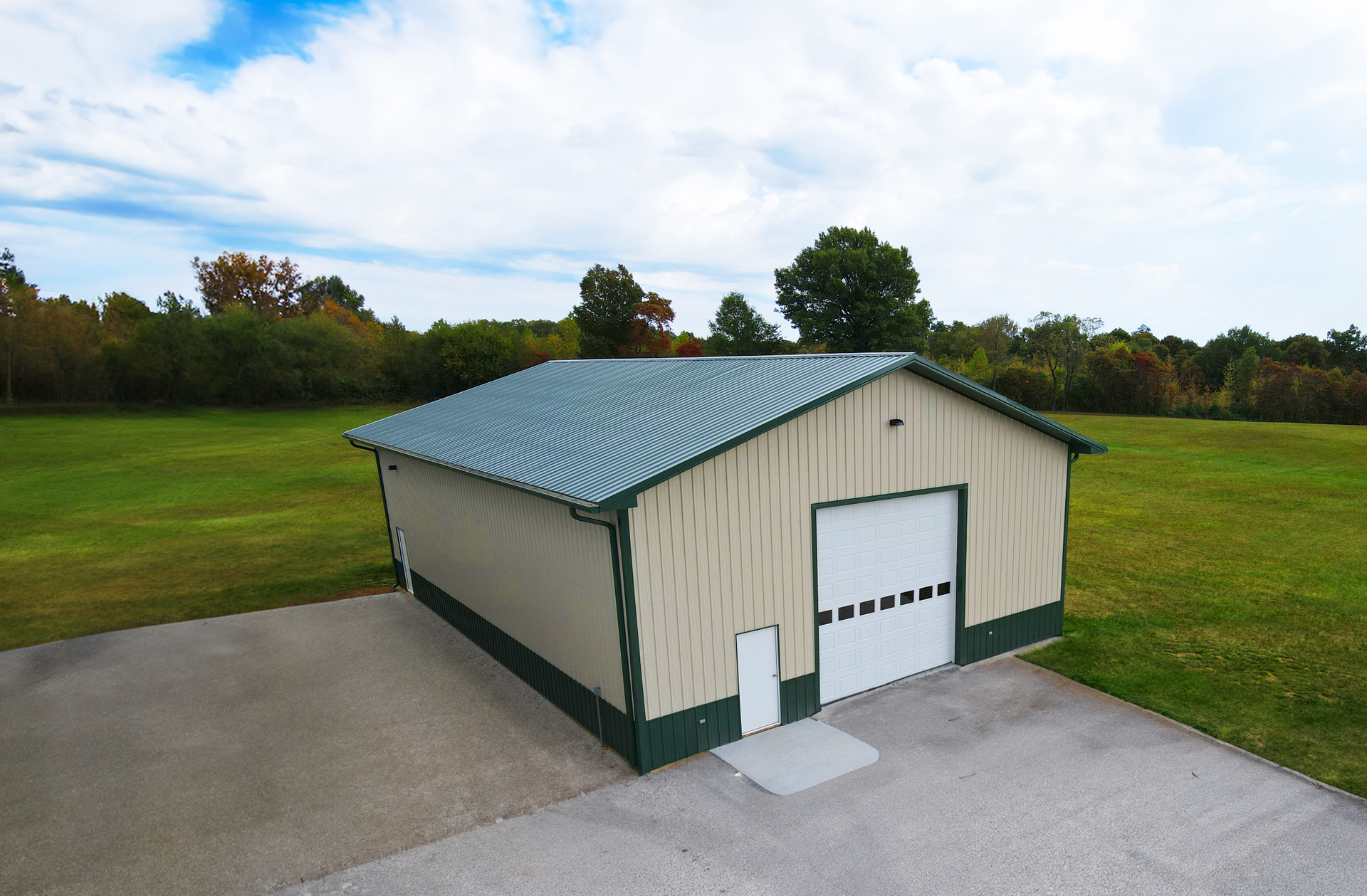 Tan metal-roofed garage with beige siding beside a paved driveway and grassy field