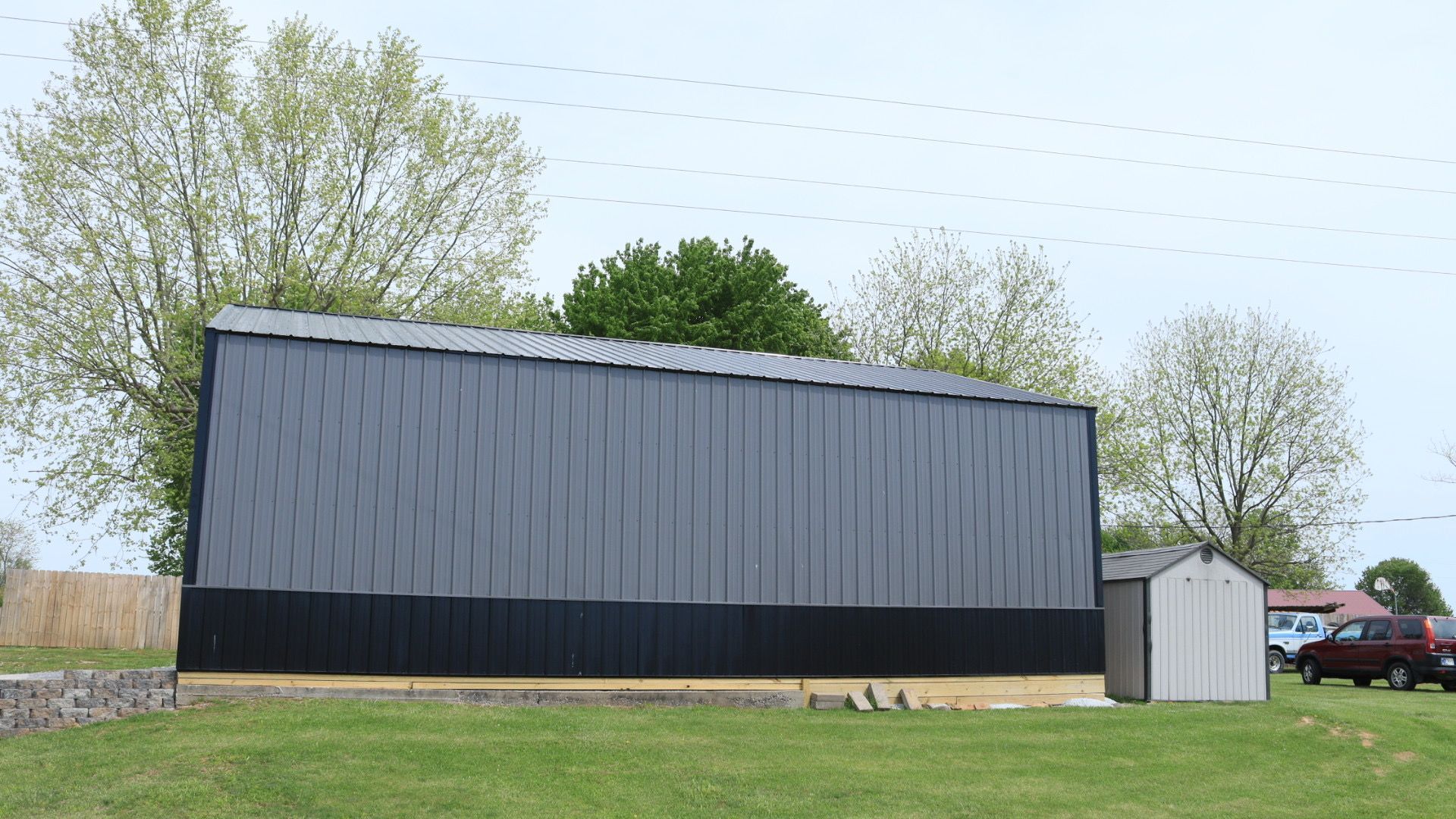 Large black barn-like building with a small white shed beside it in a grassy rural field.