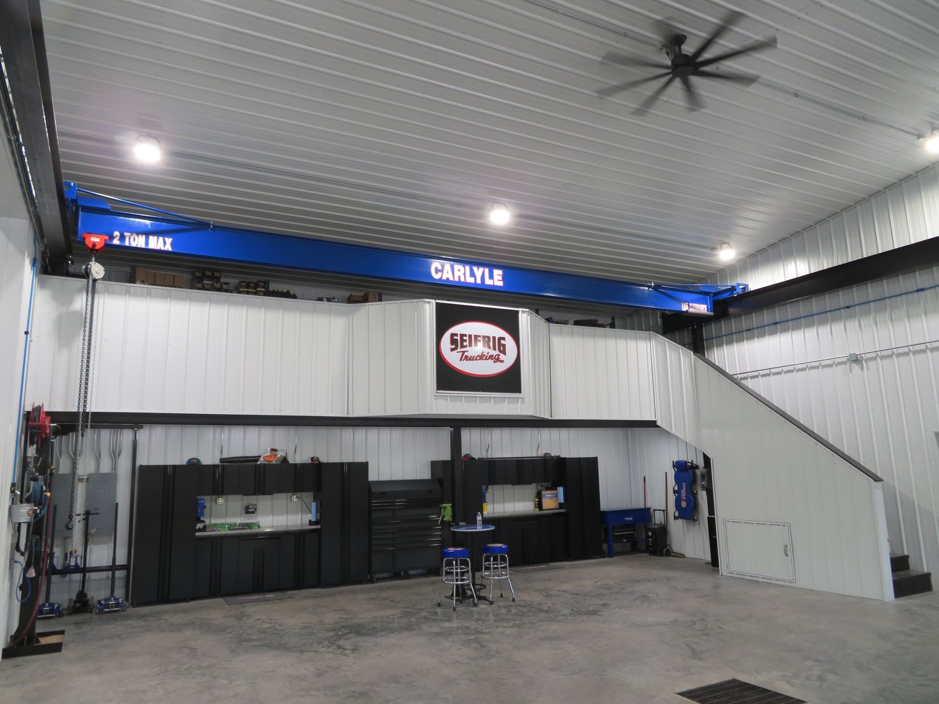 Empty indoor workshop with a loft, black cabinets, and a staircase in a white metal building