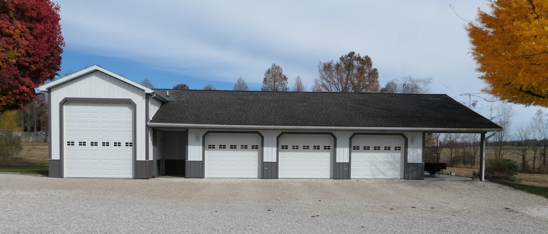 Three-door gray garage with white trim and a gravel driveway in front of a house