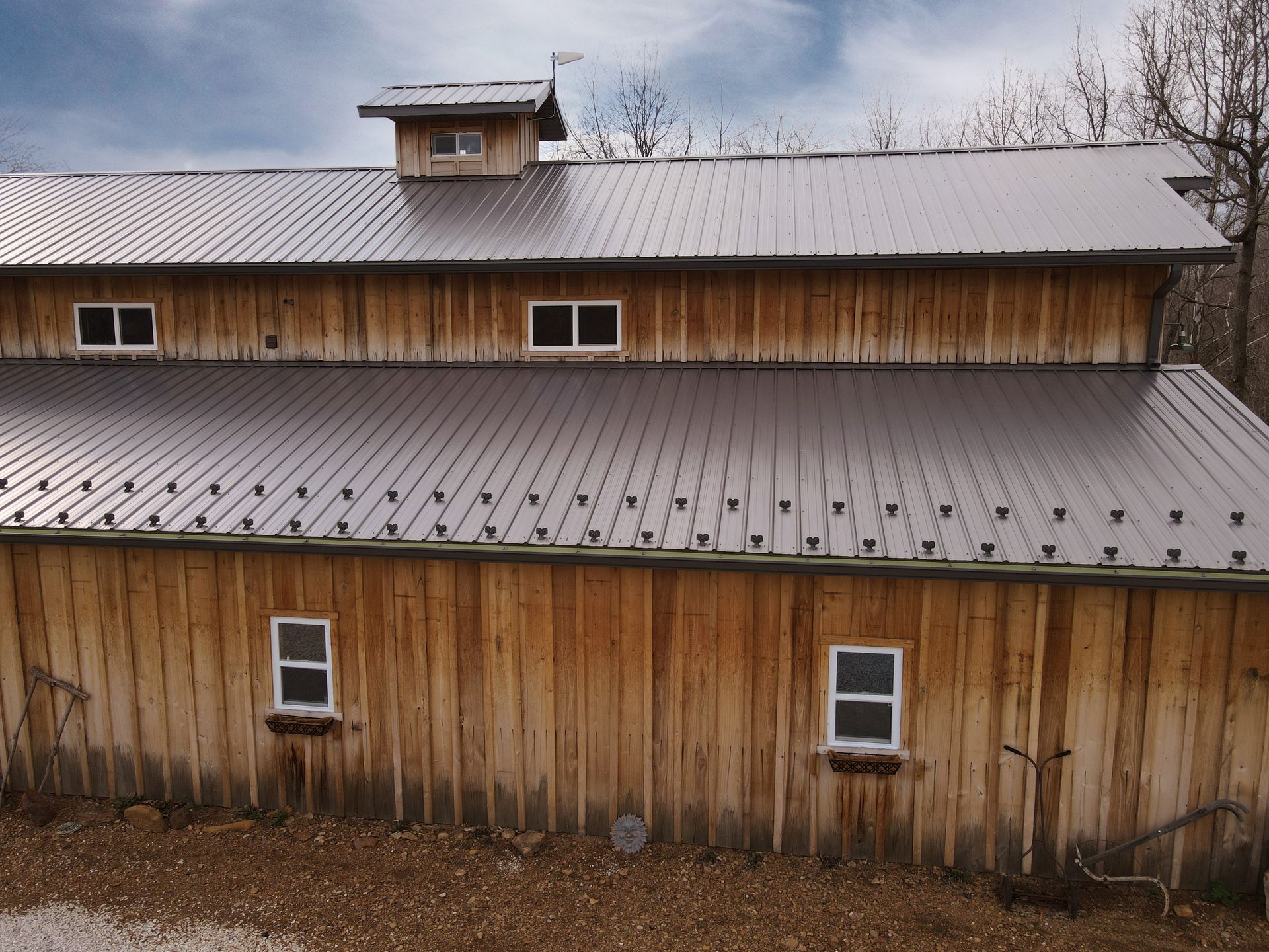 Rustic wooden barn with metal roofs and small windows under a cloudy sky.