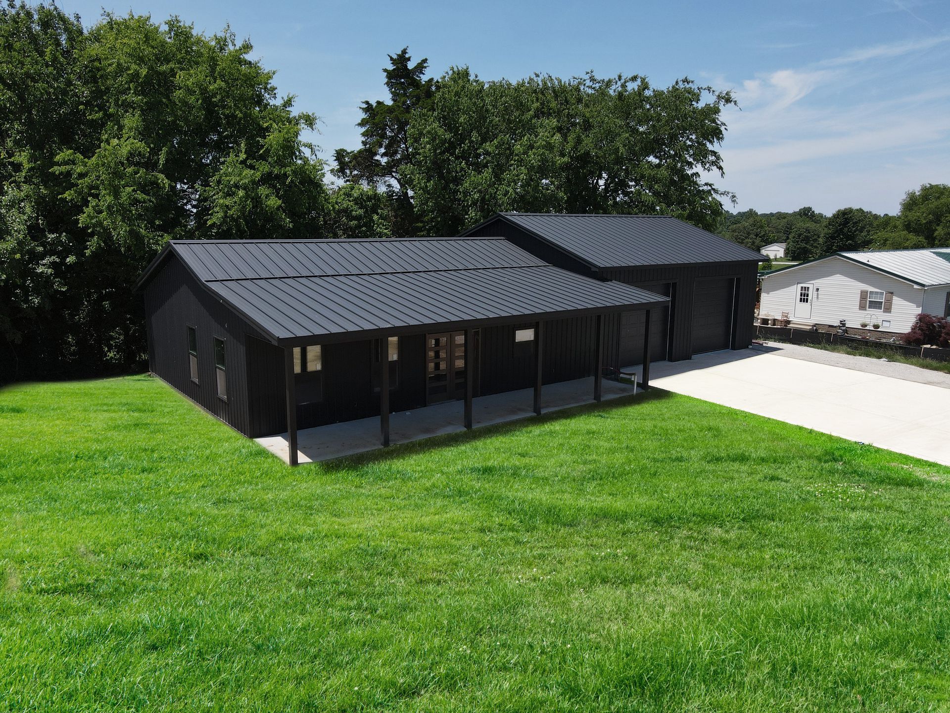 Black house with screened porch and attached garage on a grassy lawn under a blue sky.