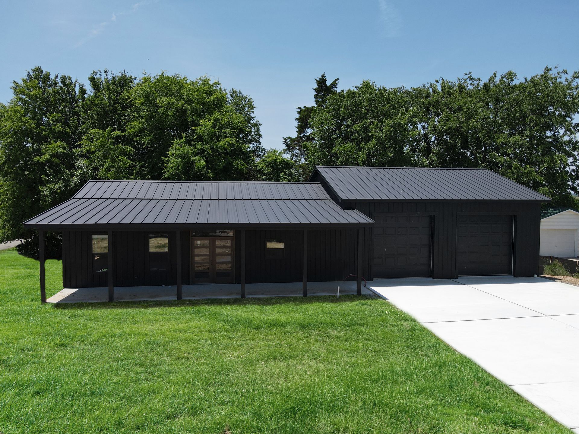 Dark wooden garage or workshop building with a metal roof beside a concrete driveway and green lawn