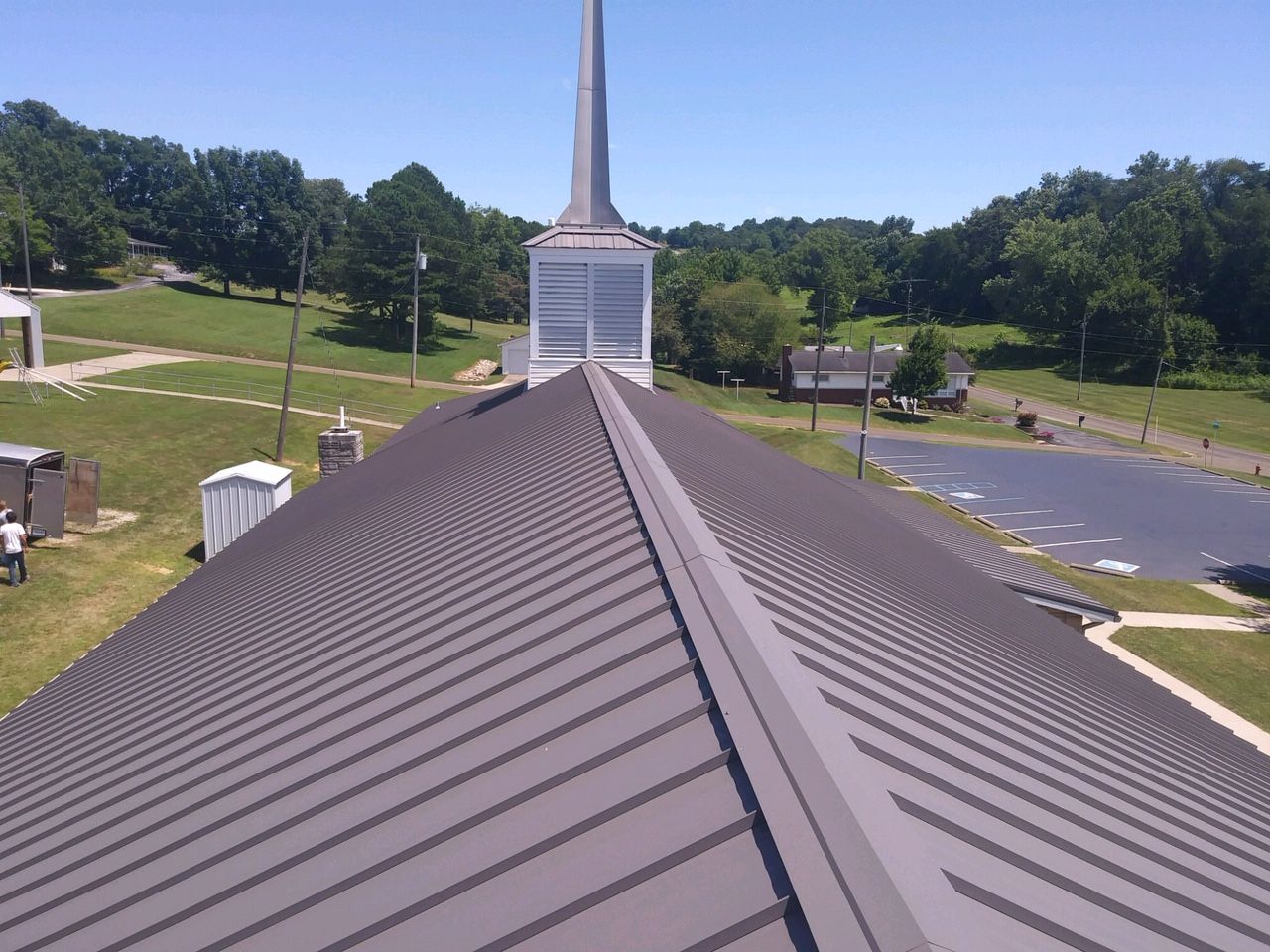 View from a church roof toward a steeple and parking lot on a sunny day
