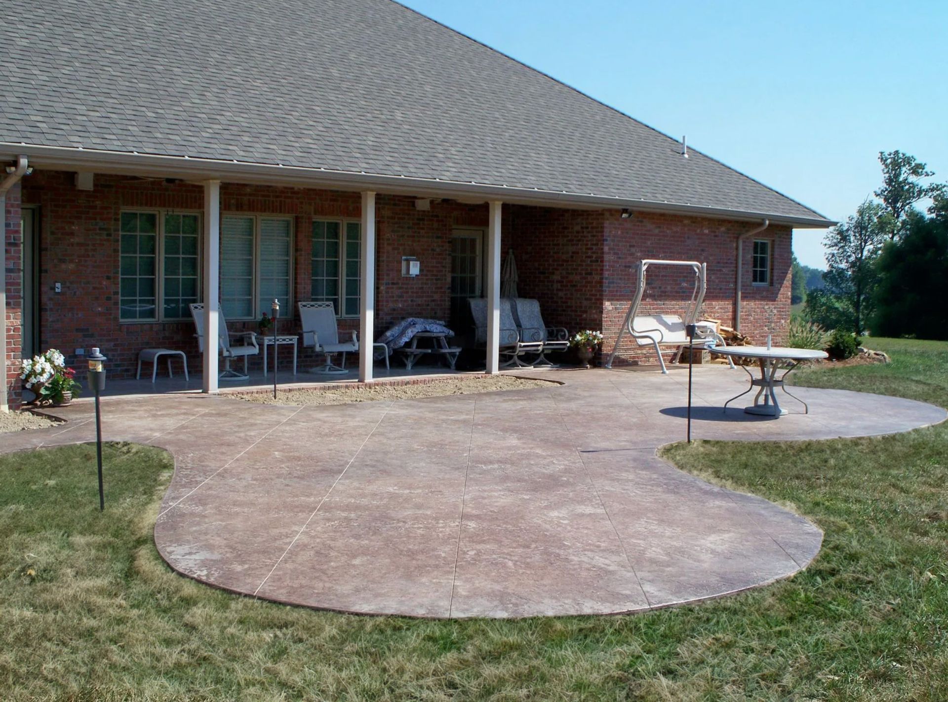 Brick house patio with outdoor chairs, grill, and a large concrete patio in a grassy yard