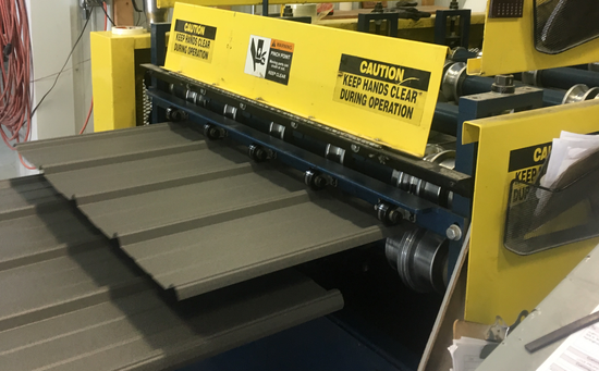 Yellow industrial sheet metal rolling machine shaping gray metal panels in a factory