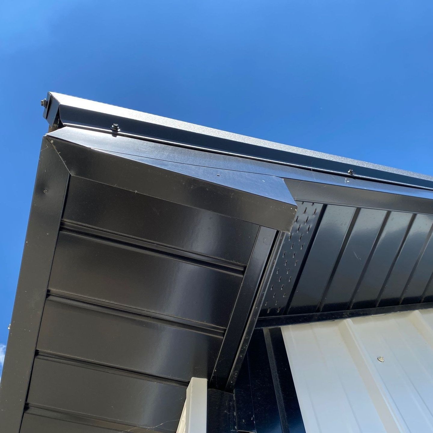Close-up of a black metal roof overhang against a bright blue sky