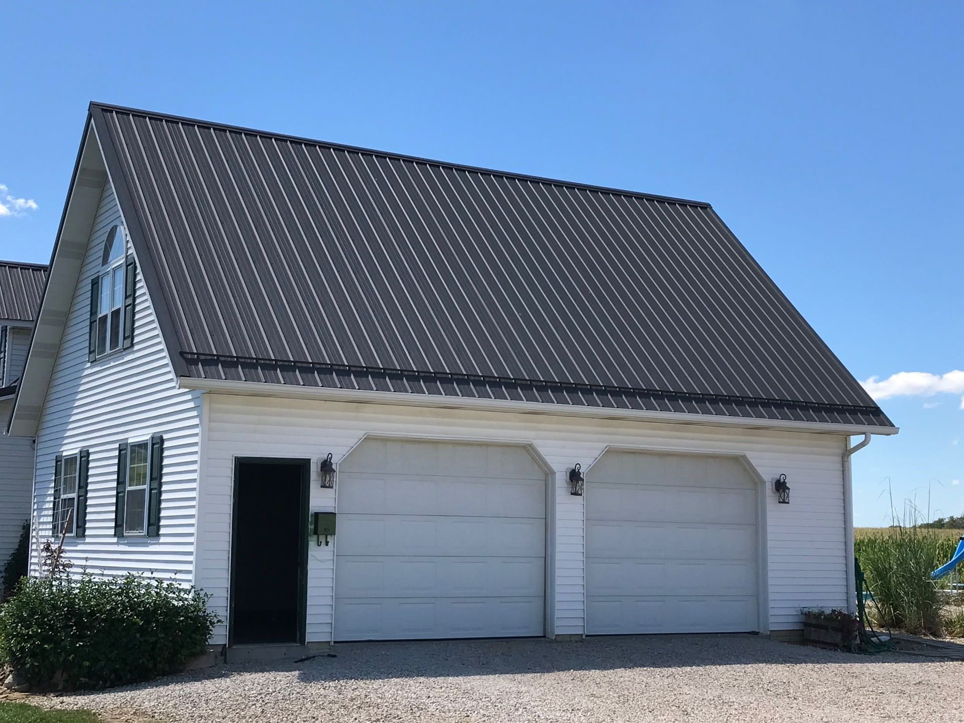 White house with a steep dark roof, two garage doors, and an open side door under a blue sky.