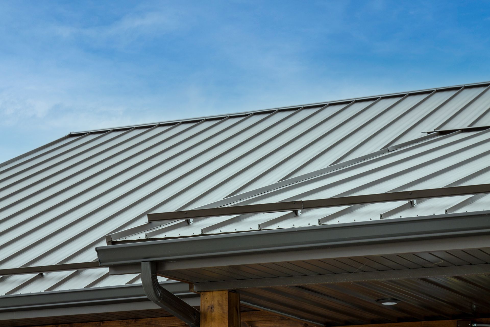 Metal roof with skylights and a gutter against a blue sky